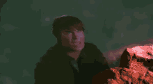 a man is standing next to a red rock and making a face