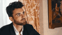 a man in a suit is sitting in front of a painting on the wall