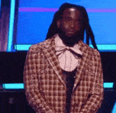 a man with dreadlocks is wearing a plaid jacket with pearls on the sleeves .