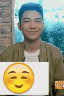 a young man is smiling and holding a picture of a smiley face