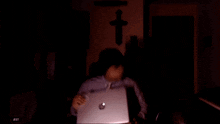 a person is using a laptop in a dark room with a cross on the wall
