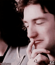 a close up of a man 's face with his hand to his mouth .