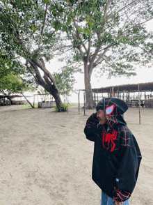a person wearing a spider-man hoodie stands in a dirt field