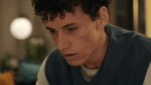 a young man with curly hair is wearing a blue vest and white shirt