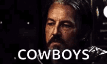 a man with a beard is looking at the camera with the words `` shit , cowboys '' written on his face .