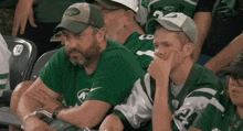 a man wearing a jets hat sits next to another man