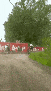 a group of people are riding dirt bikes on a dirt road in front of a sign that says lotto .
