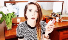 a woman in a black and white striped shirt is holding a lipstick in front of a mirror .