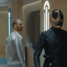 a man in a grey jacket stands next to a man in a helmet