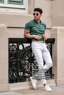 a man in a green shirt and white pants leaning against a railing