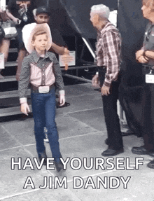 a young boy in a cowboy outfit is standing next to a man in a plaid shirt and talking to him .