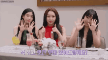 three girls are sitting at a table with drinks and flowers and giving a thumbs up sign