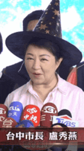 a woman wearing a witch hat stands in front of a row of microphones including tbs