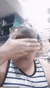 a man in a striped tank top is covering his face with his hands