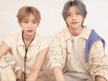 two young men are sitting next to each other with one wearing a blue sweater