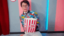 a man in glasses is holding a striped bucket of popcorn .