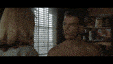 a shirtless man is looking at a woman in front of a window