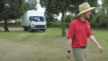 a man wearing a hat and a red shirt walks in front of a truck