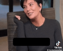 a woman in a black shirt is sitting in a chair with a tiktok logo on the bottom right