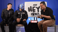 three men sit in front of a sign that says " hey "