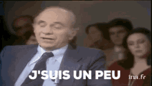 a man in a suit and tie says j 'suis un peu in front of a crowd of people