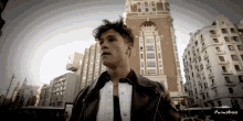 a man in a leather jacket is standing in front of a tall building with the name itansboo on the bottom