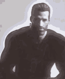a man with a beard wearing a black shirt is standing in a dark room