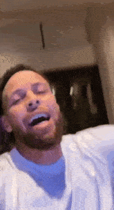 a man with a beard and a white shirt is laughing with his eyes closed .