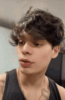 a young man with curly hair is wearing a black tank top and a necklace .