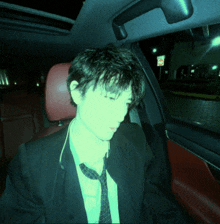 a man in a suit and tie sits in the back seat of a car with a no parking sign in the background