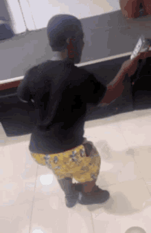 a man in a black shirt and yellow shorts is standing on a tiled floor holding a remote control .