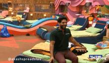 a man in a green shirt is sitting on a bed in a room that says imgplay