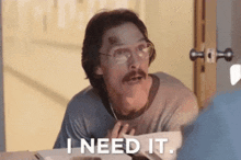 a man with glasses and a mustache is sitting at a table and says i need it .