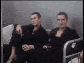 two men are sitting on a couch and one is holding a glass