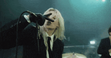a woman singing into a microphone while wearing a black suit and tie