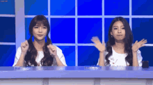 two girls are sitting at a table with their hands up in the air .
