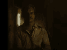 a man in a shirt and tie is sitting in a dark room looking at the camera .