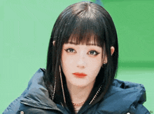 a woman with black hair and bangs is wearing a black jacket and earrings .