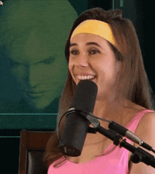 a woman wearing a pink tank top and a yellow headband is smiling into a microphone .