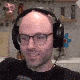 a bald man with glasses is wearing headphones and smiling .