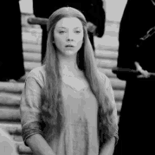 a black and white photo of a woman with long hair standing in front of a group of people .