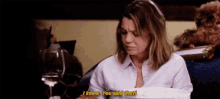 a woman is sitting at a table with a glass of wine talking to another woman .