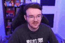 a man with glasses and a beard is sitting in a chair in front of a computer screen .