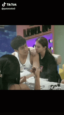 a man and a woman are kissing while sitting at a table in front of a sign that says level up .