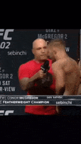 a man in a red shirt is holding a microphone and talking to another man in a red shirt