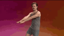 a man in a tank top and shorts is dancing in front of a pink background .