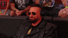 a man wearing sunglasses and headphones sits in a stadium with a shirt that says u on it