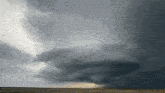 a storm is coming in over a field with a few trees in the distance