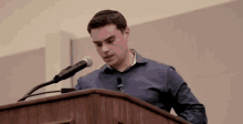 a man is standing at a podium speaking into a microphone .