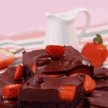 a piece of chocolate cake with strawberries on top and a pitcher in the background